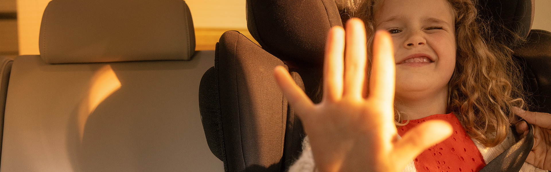 Kind sitzt im Auto und hält Hand in die Kamera